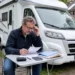 Camperbezitter bekijkt papieren en kostenoverzicht naast een geparkeerde camper.